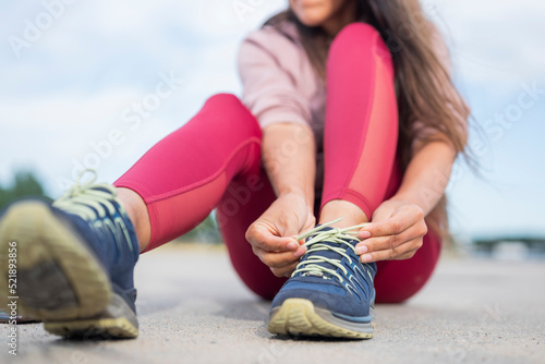 girl soprtsman sits on the pavement and ties shoelaces on sneakers photo