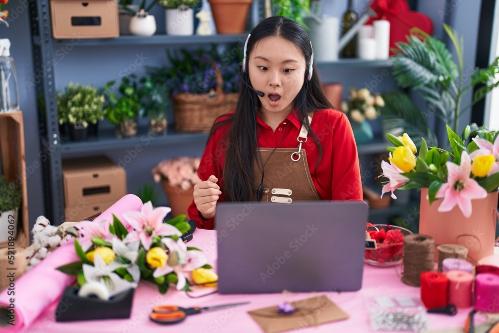 Young asian woman working at florist shop doing video call scared and amazed with open mouth for surprise, disbelief face