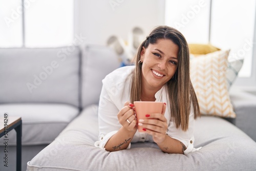 Young hispanic woman drinking coffee lying on sofa at home