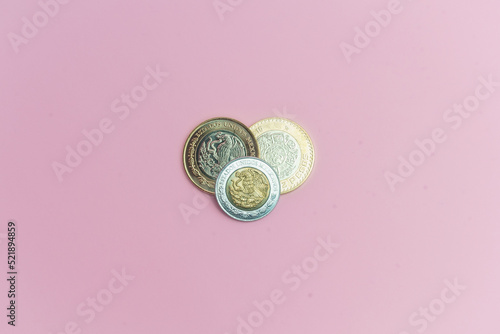 Dos monedas de 10 pesos mexicanos y moneda de 2 pesos mexicanos sobre fondo rosa.