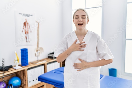 Young caucasian woman working at pain recovery clinic smiling and laughing hard out loud because funny crazy joke with hands on body.