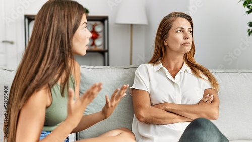 Mother and daughter unhappy arguing sitting on sofa at home photo
