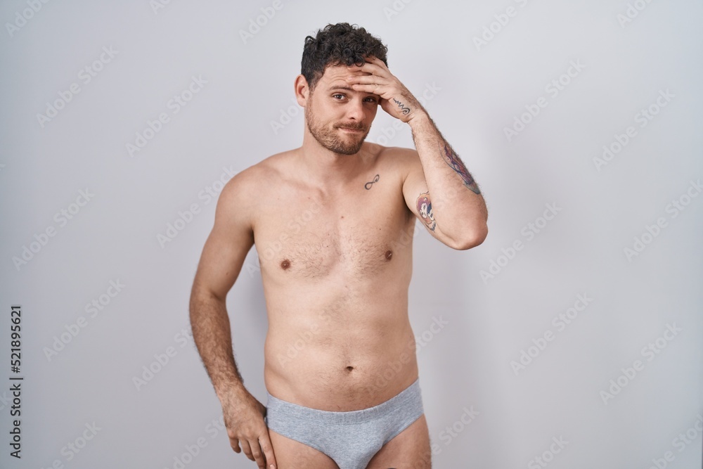 Fototapeta premium Young hispanic man standing shirtless wearing underware worried and stressed about a problem with hand on forehead, nervous and anxious for crisis