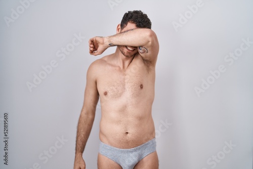 фотографія Young hispanic man standing shirtless wearing underware covering eyes with arm smiling cheerful and funny