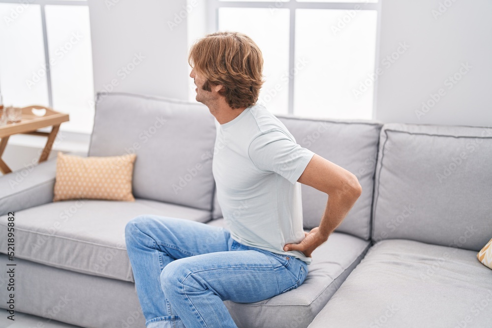 Young man suffering for back ache sitting on sofa at home