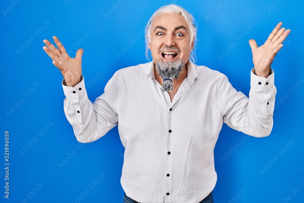 Middle age man with grey hair standing over blue background celebrating crazy and amazed for success with arms raised and open eyes screaming excited. winner concept Middle age man with grey hair standing over blue background celebrating crazy and amazed for success with arms raised and open eyes screaming excited. winner concept