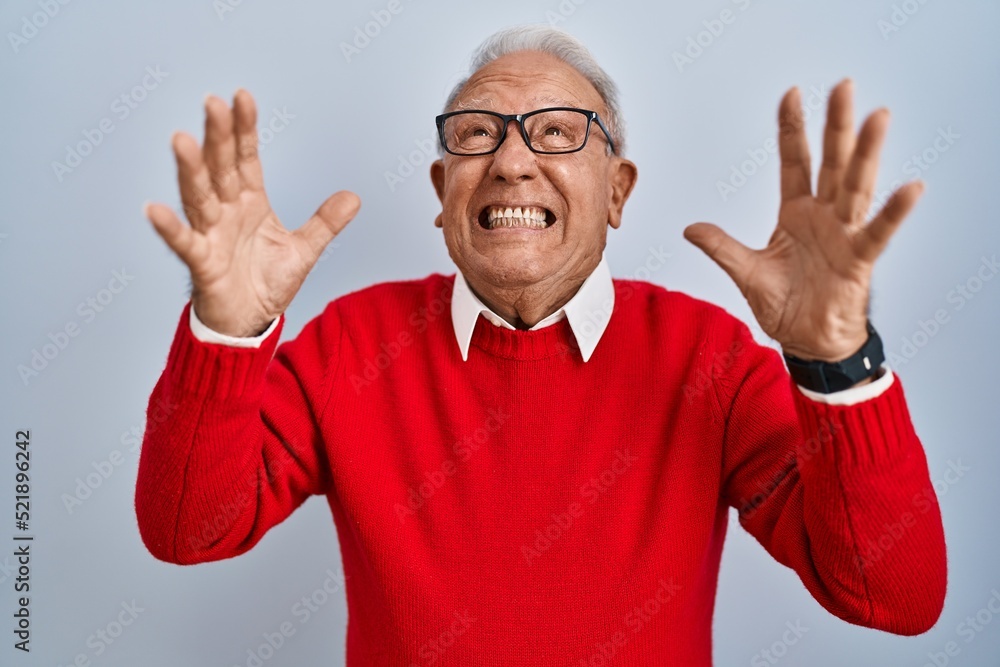 Senior man with grey hair standing over isolated background crazy and mad shouting and yelling with aggressive expression and arms raised. frustration concept. Senior man with grey hair standing over isolated background crazy and mad shouting and yelling with aggressive expression and arms raised. frustration concept.