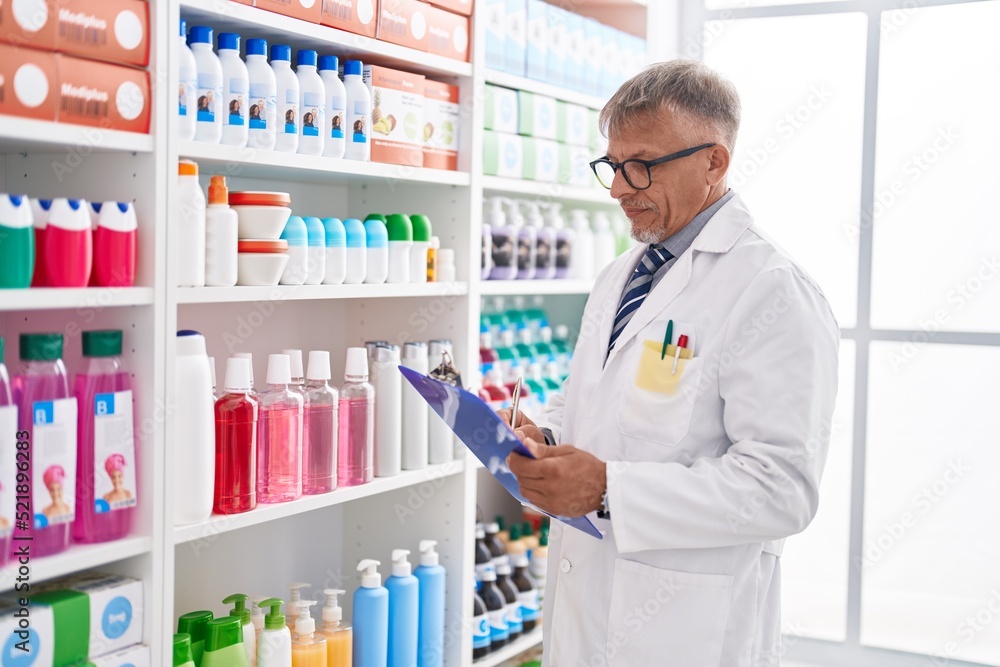 Middle age grey-haired man pharmacist writing on document at laboratory