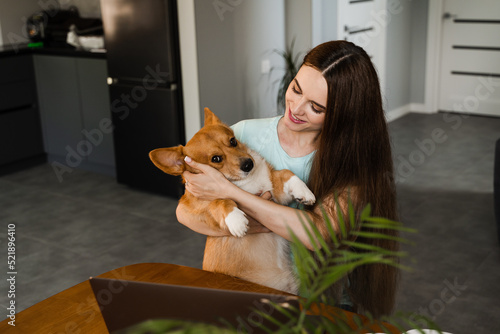 Lifestryle of girl freelancer and domestic Corgi dog at home. Working at home with laptop. Girl hug and play with lovely Welsh Corgi Pembroke in break at online work.