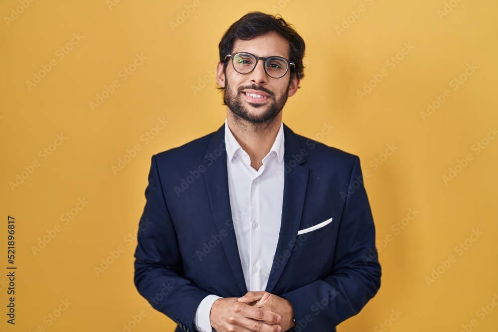 Handsome latin man standing over yellow background with hands together and crossed fingers smiling relaxed and cheerful. success and optimistic Handsome latin man standing over yellow background with hands together and crossed fingers smiling relaxed and cheerful. success and optimistic