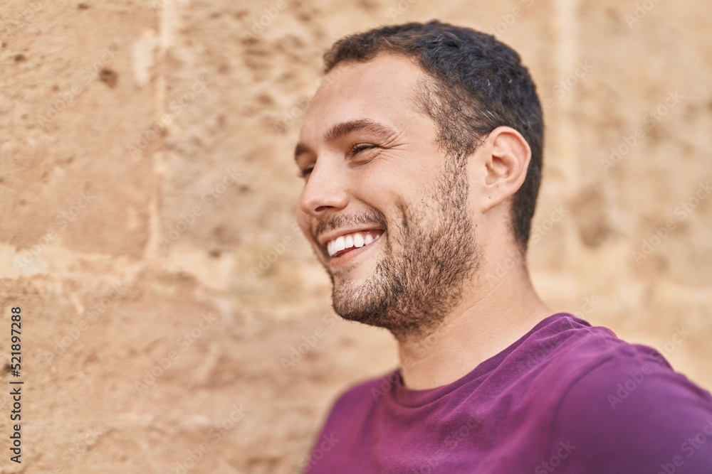 Fototapeta premium Young man smiling confident looking to the side over isolated brick background
