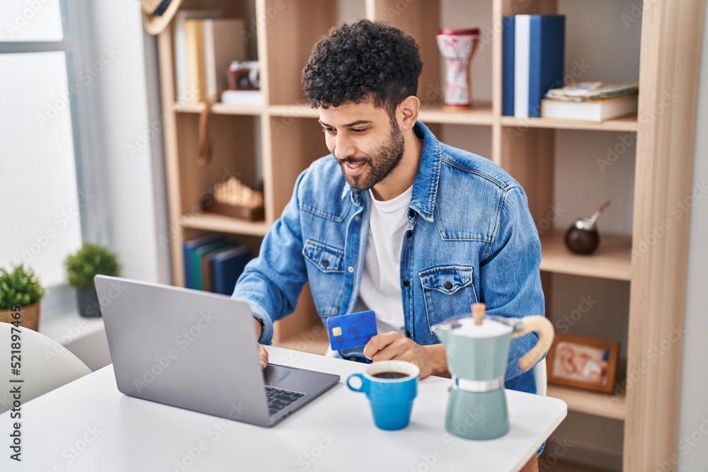 Young arab man using laptop and credit card sitting on table at home Young arab man using laptop and credit card sitting on table at home