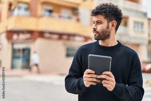 Young arab man with relaxed expression using touchpad at street