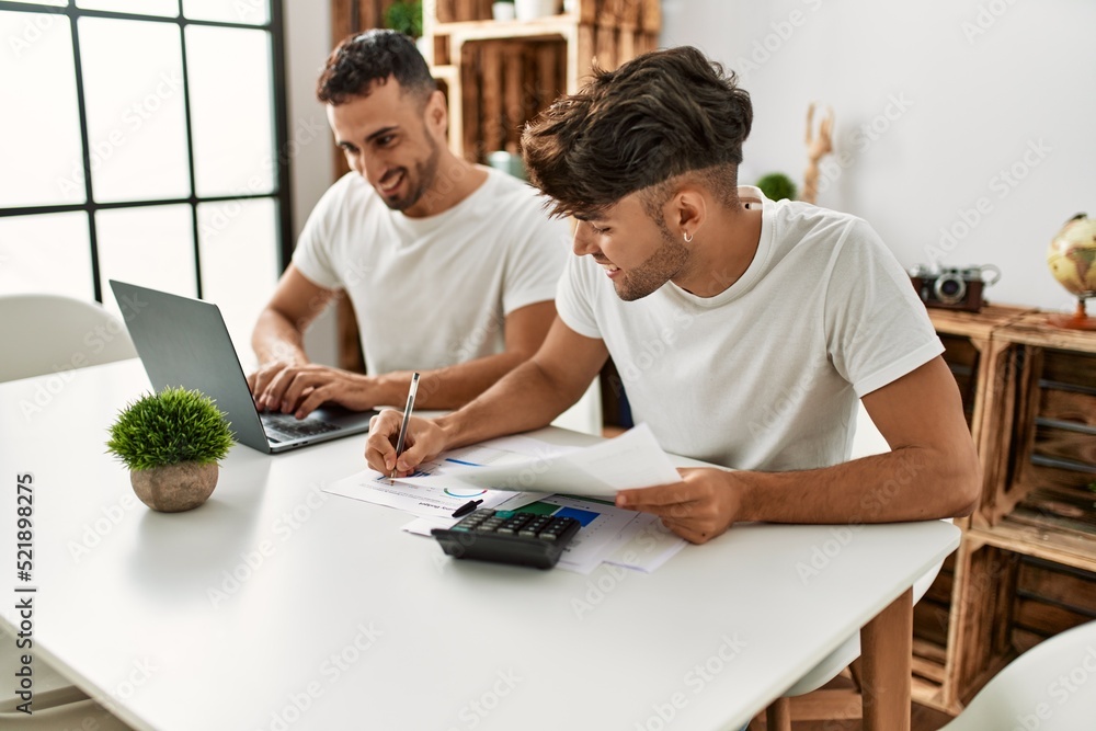 Obraz premium Two hispanic men couple smiling confident using laptop working at home