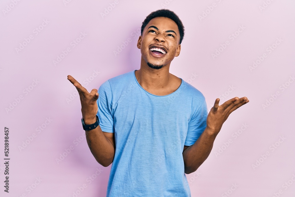 Young african american man wearing casual blue t shirt crazy and mad shouting and yelling with aggressive expression and arms raised. frustration concept. Young african american man wearing casual blue t shirt crazy and mad shouting and yelling with aggressive expression and arms raised. frustration concept.