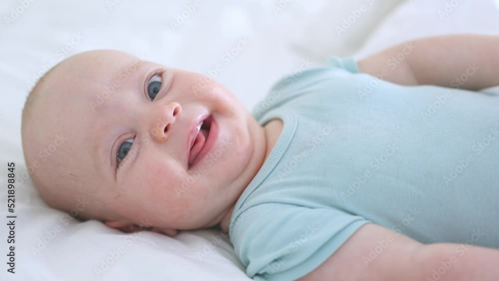 beautiful baby lying in bed, looking to camera, happy blue eyed caucasian infant in white bedroom, sunny morning. 3 months infant playing active leisure activity indoors. morning time family lifestyle beautiful baby lying in bed, looking to camera, happy blue eyed caucasian infant in white bedroom, sunny morning. 3 months infant playing active leisure activity indoors. morning time family lifestyle