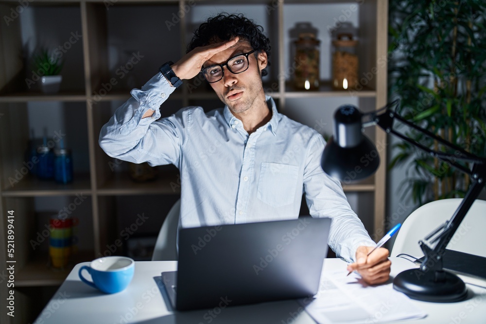 Obraz premium Hispanic man working at the office at night worried and stressed about a problem with hand on forehead, nervous and anxious for crisis