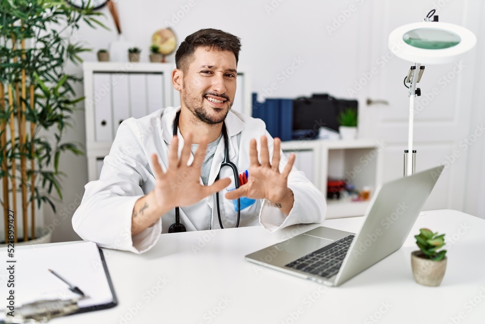 Young doctor working at the clinic using computer laptop afraid and terrified with fear expression stop gesture with hands, shouting in shock. panic concept. Young doctor working at the clinic using computer laptop afraid and terrified with fear expression stop gesture with hands, shouting in shock. panic concept.