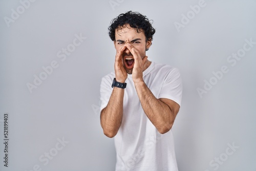 Hispanic man standing over isolated background shouting angry out loud with hands over mouth