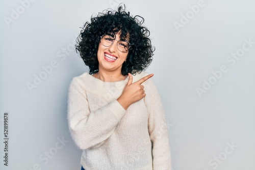 Young middle east woman wearing casual white tshirt cheerful with a smile of face pointing with hand and finger up to the side with happy and natural expression on face