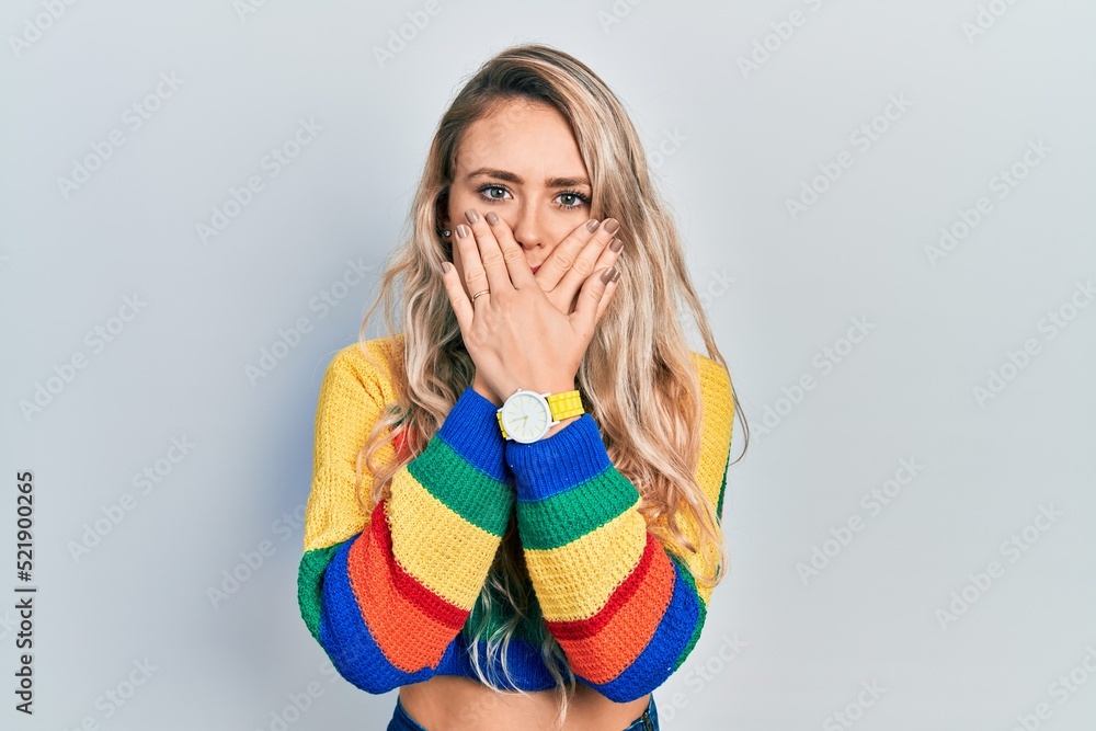 Beautiful young blonde woman wearing colored sweater shocked covering mouth with hands for mistake. secret concept. Beautiful young blonde woman wearing colored sweater shocked covering mouth with hands for mistake. secret concept.