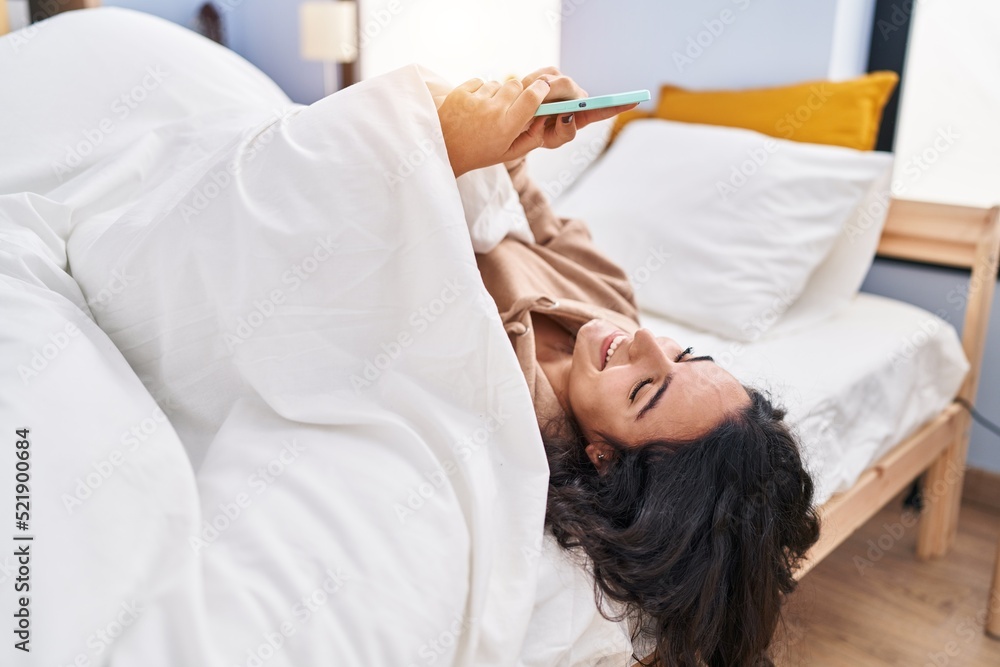 Young hispanic woman using smartphone lying on bed at bedroom Young hispanic woman using smartphone lying on bed at bedroom