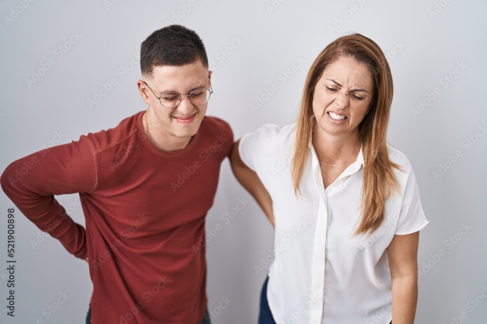 Mother and son standing together over isolated background suffering of backache, touching back with hand, muscular pain Mother and son standing together over isolated background suffering of backache, touching back with hand, muscular pain