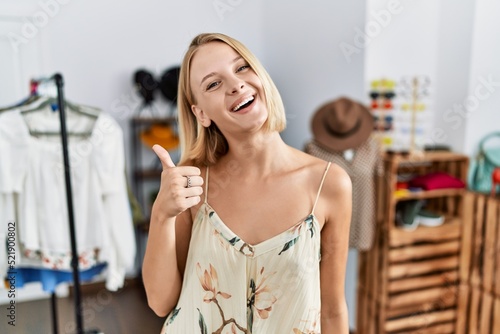 Young caucasian woman at retail shop doing happy thumbs up gesture with hand. approving expression looking at the camera showing success.