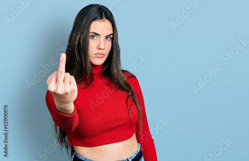 Young brunette teenager wearing red turtleneck sweater showing middle finger, impolite and rude fuck off expression