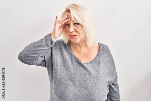 Middle age caucasian woman standing over white background worried and stressed about a problem with hand on forehead, nervous and anxious for crisis