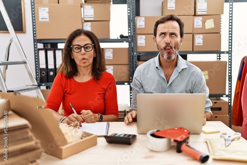 Middle age couple working at small business ecommerce making fish face with lips, crazy and comical gesture. funny expression.