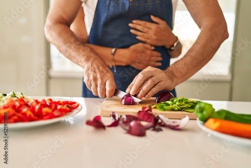 Middle age hispanic couple hugging each other cooking at kitchen