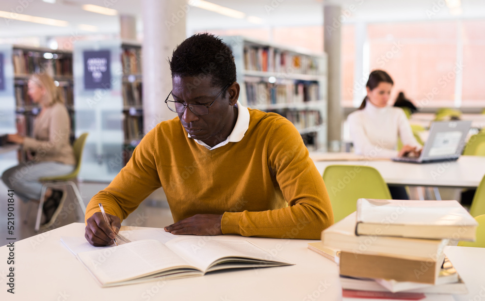 Portrait of confident african-american male student working with book in public library. High quality photo