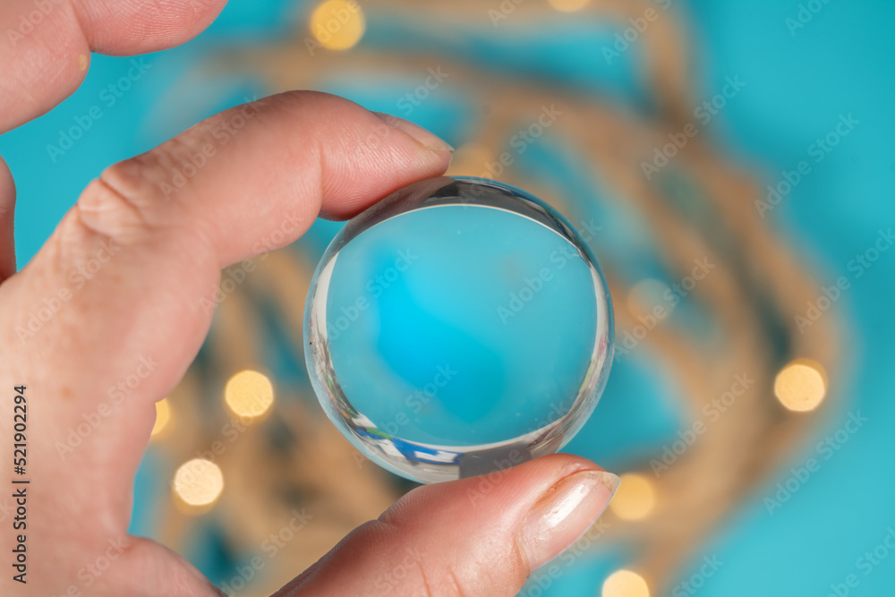 main tenant une bille de verre transparente au dessus d'une table bleue avec une corde main tenant une bille de verre transparente au dessus d'une table bleue avec une corde