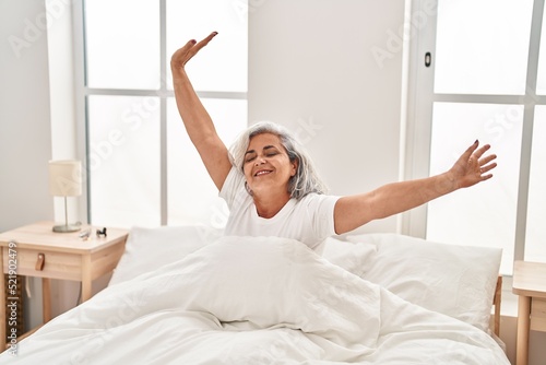 Middle age woman waking up stretching arms at bedroom