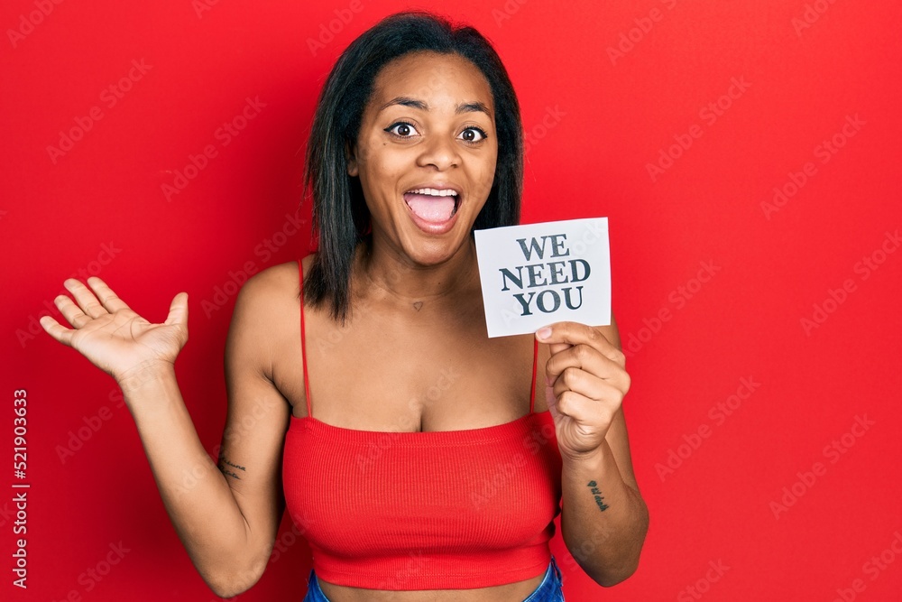Young african american girl holding we need you paper celebrating victory with happy smile and winner expression with raised hands Young african american girl holding we need you paper celebrating victory with happy smile and winner expression with raised hands