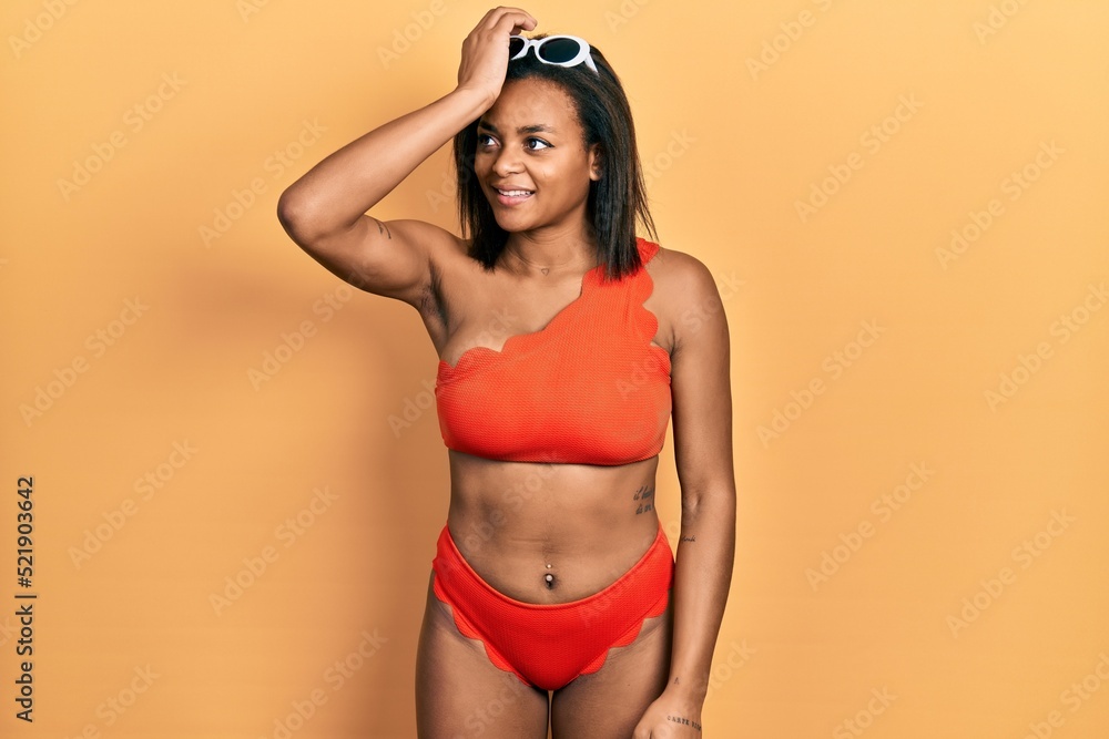 Young african american girl wearing bikini smiling confident touching hair with hand up gesture, posing attractive and fashionable Young african american girl wearing bikini smiling confident touching hair with hand up gesture, posing attractive and fashionable