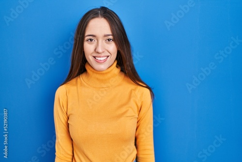 Young brunette woman standing over blue background with a happy and cool smile on face. lucky person.