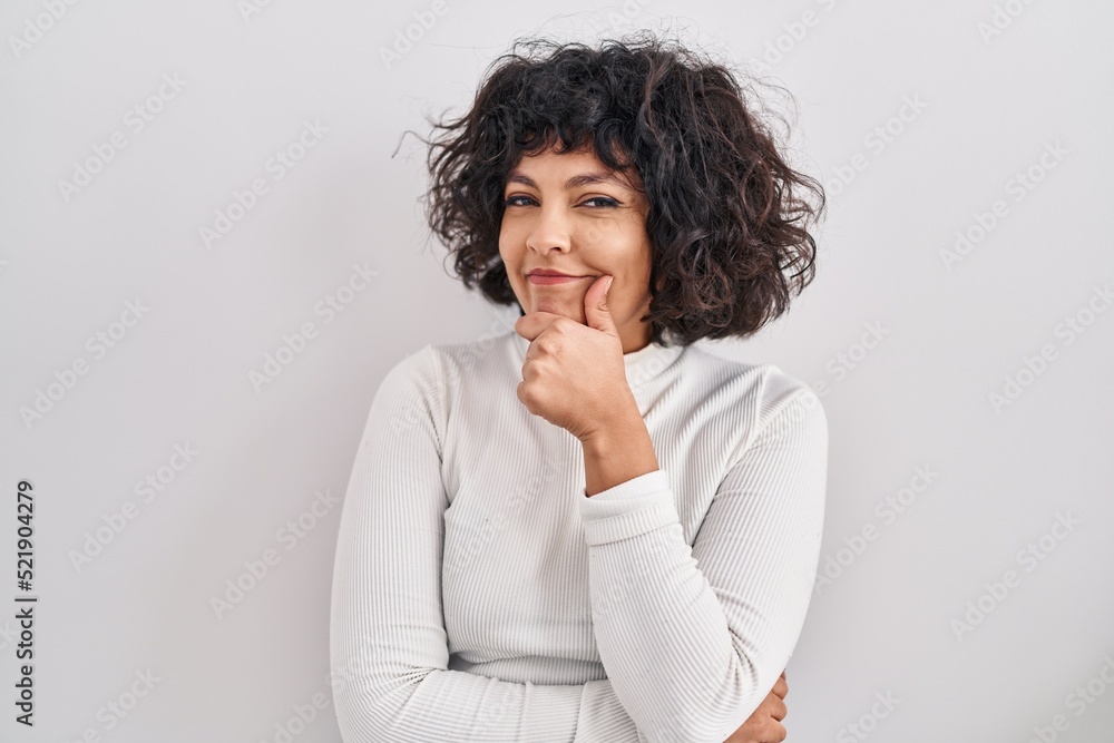 Hispanic woman with curly hair standing over isolated background looking confident at the camera smiling with crossed arms and hand raised on chin. thinking positive. Hispanic woman with curly hair standing over isolated background looking confident at the camera smiling with crossed arms and hand raised on chin. thinking positive.