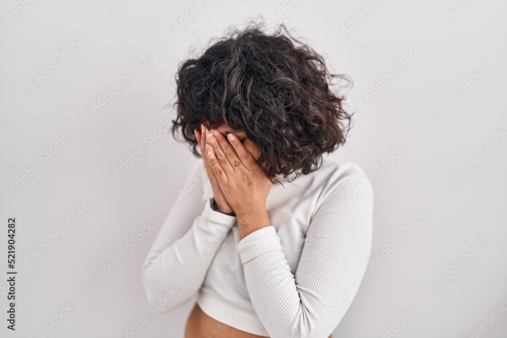 Hispanic woman with curly hair standing over isolated background with sad expression covering face with hands while crying. depression concept. Hispanic woman with curly hair standing over isolated background with sad expression covering face with hands while crying. depression concept.