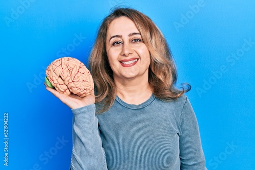 Middle age caucasian woman holding brain looking positive and happy standing and smiling with a confident smile showing teeth
