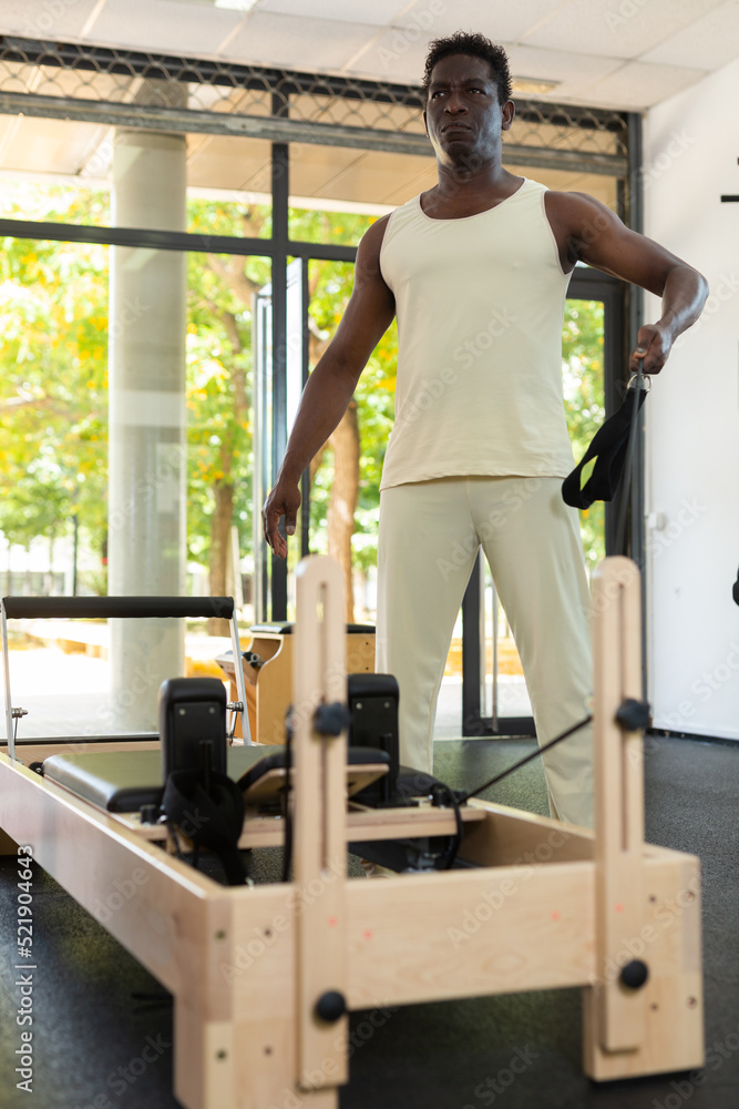 African-american man doing exercises on pilates reformer during training in gym.