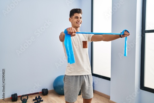 Young hispanic man smiling confident training using elastic band at sport center