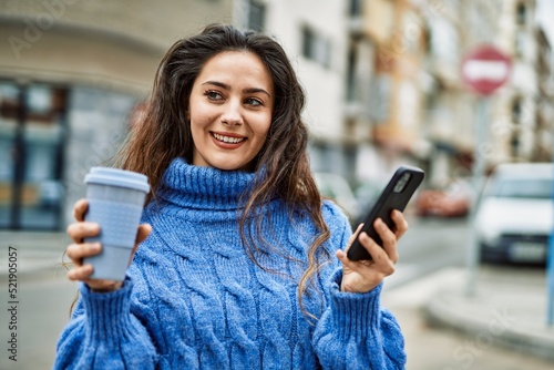 Young hispanic woman using smartphone drinking coffee at the city.