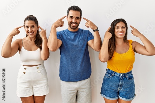 Group of young hispanic people standing over isolated background smiling pointing to head with both hands finger  great idea or thought  good memory