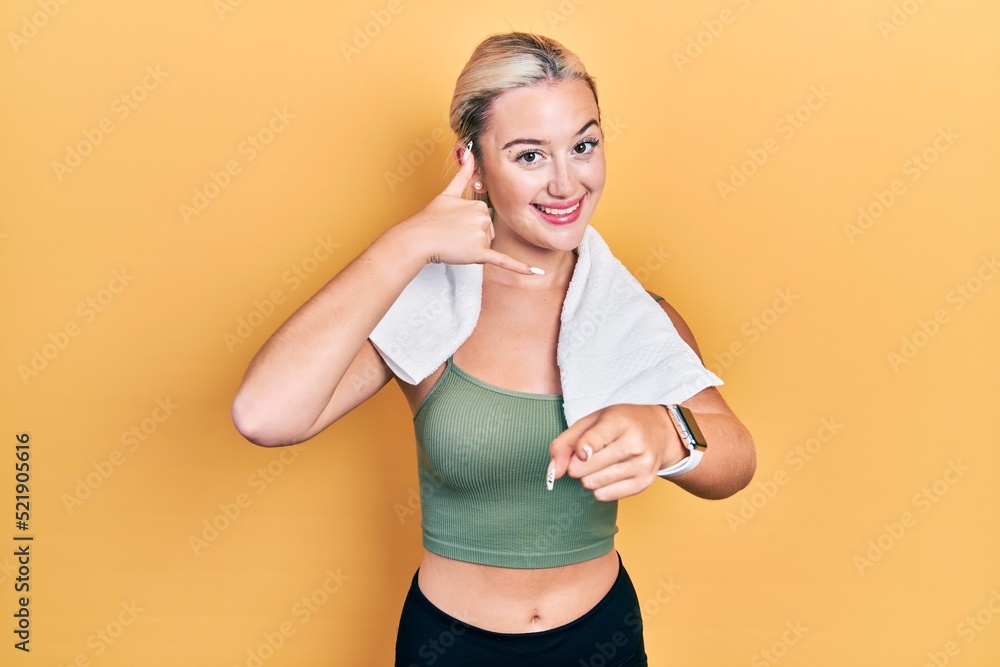 Young blonde girl wearing sportswear and towel smiling doing talking on the telephone gesture and pointing to you. call me. Young blonde girl wearing sportswear and towel smiling doing talking on the telephone gesture and pointing to you. call me.