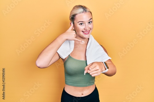 Young blonde girl wearing sportswear and towel smiling doing talking on the telephone gesture and pointing to you. call me. © Krakenimages.com