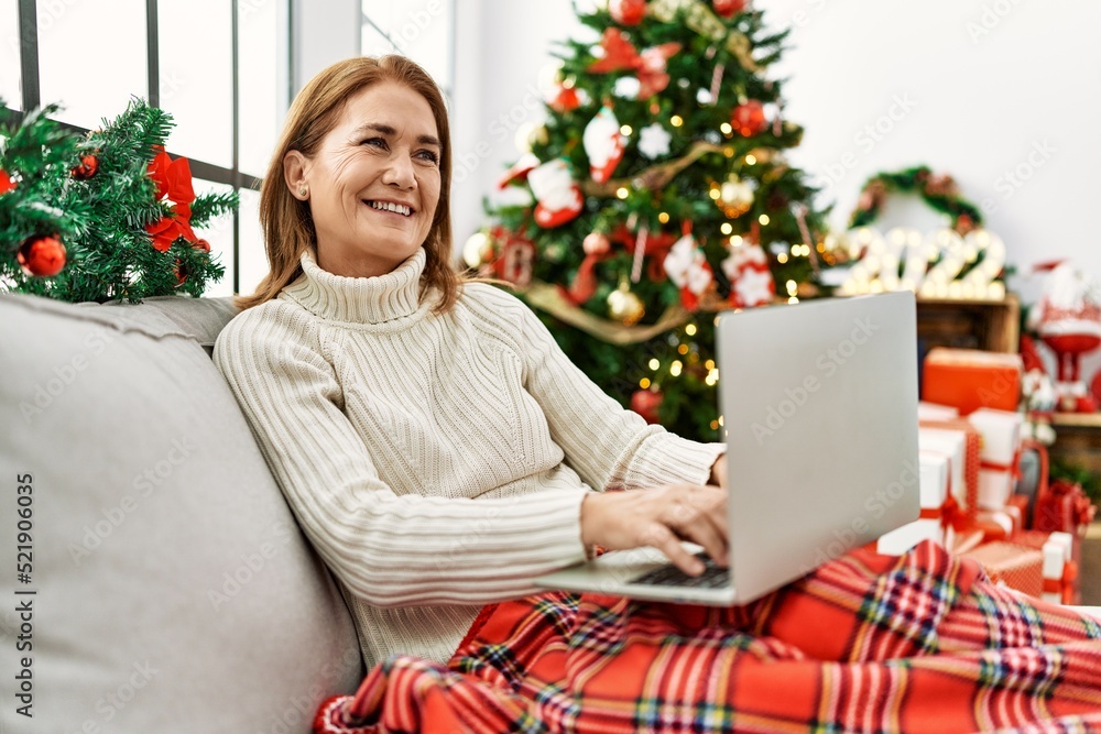 Middle age caucasian woman using laptop sitting by christmas tree at home Middle age caucasian woman using laptop sitting by christmas tree at home