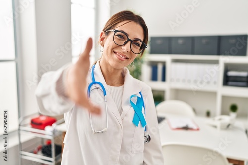 Young brunette doctor woman wearing stethoscope at the clinic smiling friendly offering handshake as greeting and welcoming. successful business.