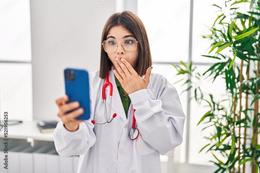Young hispanic doctor woman working on online appointment covering mouth with hand, shocked and afraid for mistake. surprised expression Young hispanic doctor woman working on online appointment covering mouth with hand, shocked and afraid for mistake. surprised expression